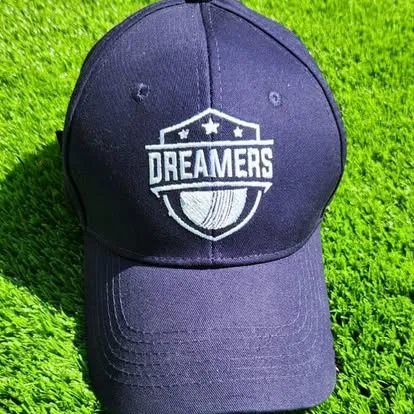 A navy Dreamers cap resting on the grass, the shield crest embroidered on the front.