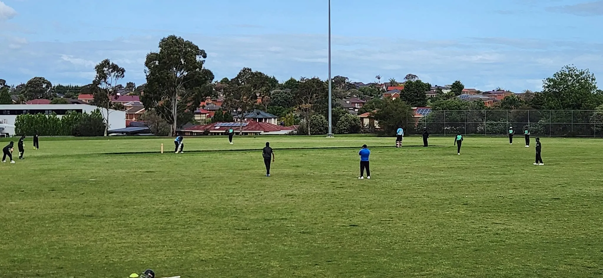 A wide view of the ground during play, fielders spread across the outfield under a blue sky.