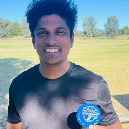 A Dreamers player smiling on the outfield, wearing the club's blue Player of the Match medal.